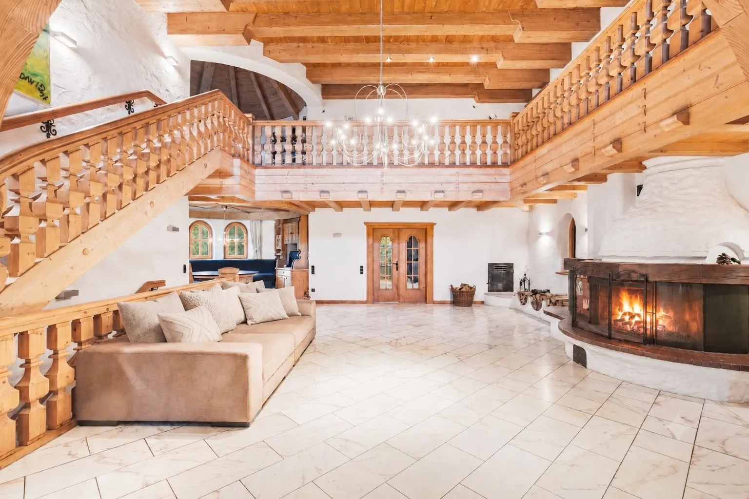Helles Wohnzimmer mit Holzbalken, Kamin, Treppe und großer Couch.