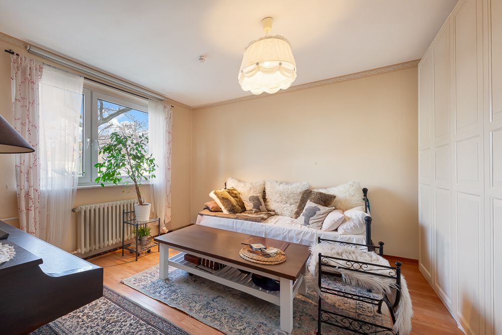 Helles Wohnzimmer mit Sofa, Couchtisch, Teppich und großem Fenster mit Vorhängen.