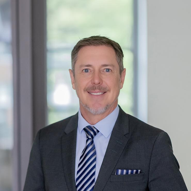 Mann im Anzug mit gestreifter Krawatte steht in einem hellen Raum.