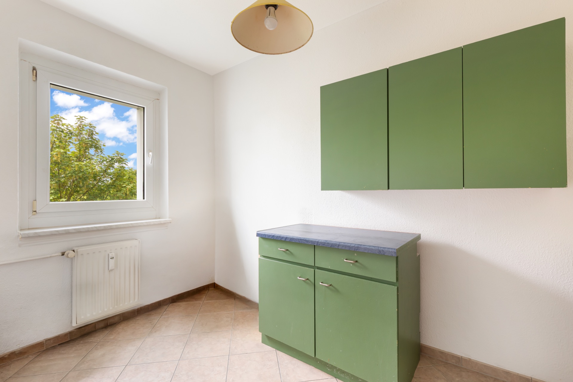 Heller Raum mit grünem Unterschrank, passenden Hängeschränken und Fenster mit Blick auf Bäume.