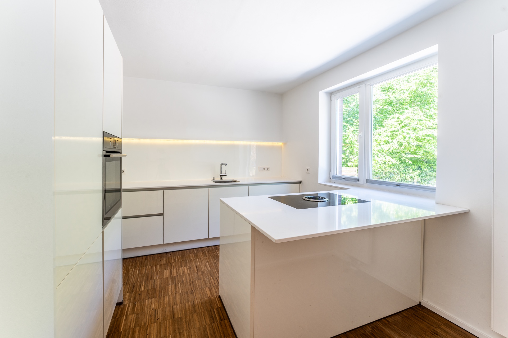 Moderne, helle Küche mit Kücheninsel, Einbauherd und großem Fenster, Holzfußboden.