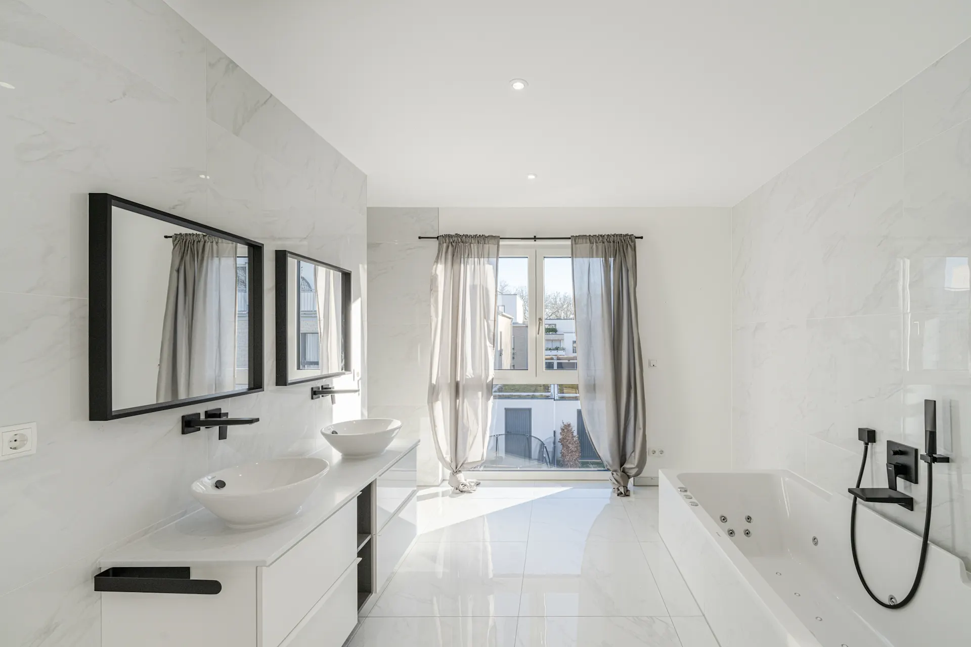 Helles Bad mit Doppelwaschbecken, großer Badewanne und Fenster mit grauen Vorhängen.