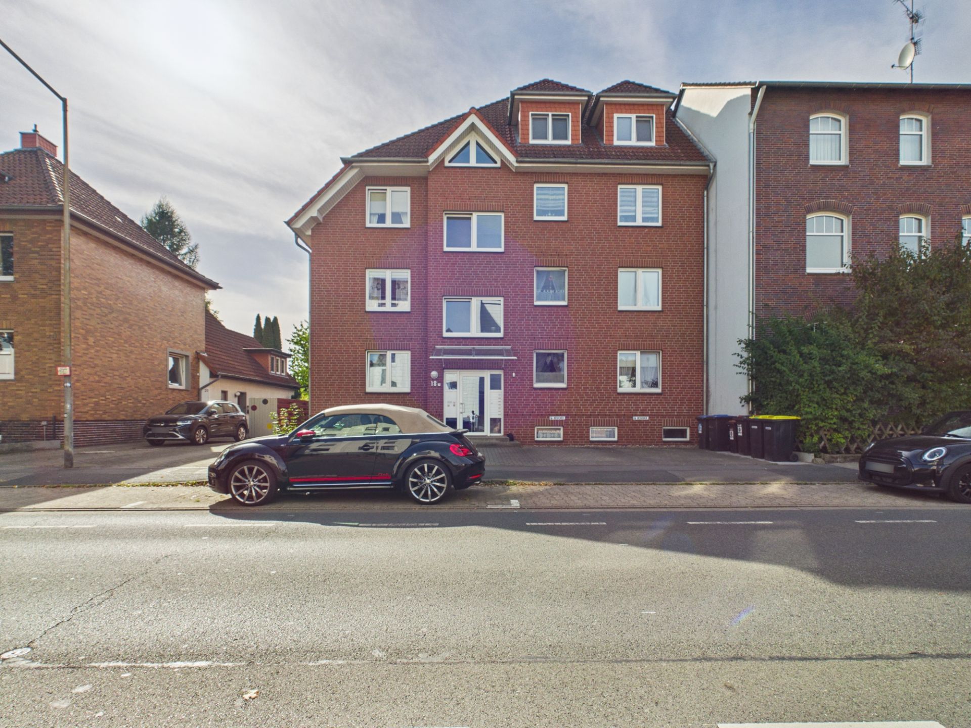 Rotes Mehrfamilienhaus mit mehreren Fenstern und geparkten Autos davor.