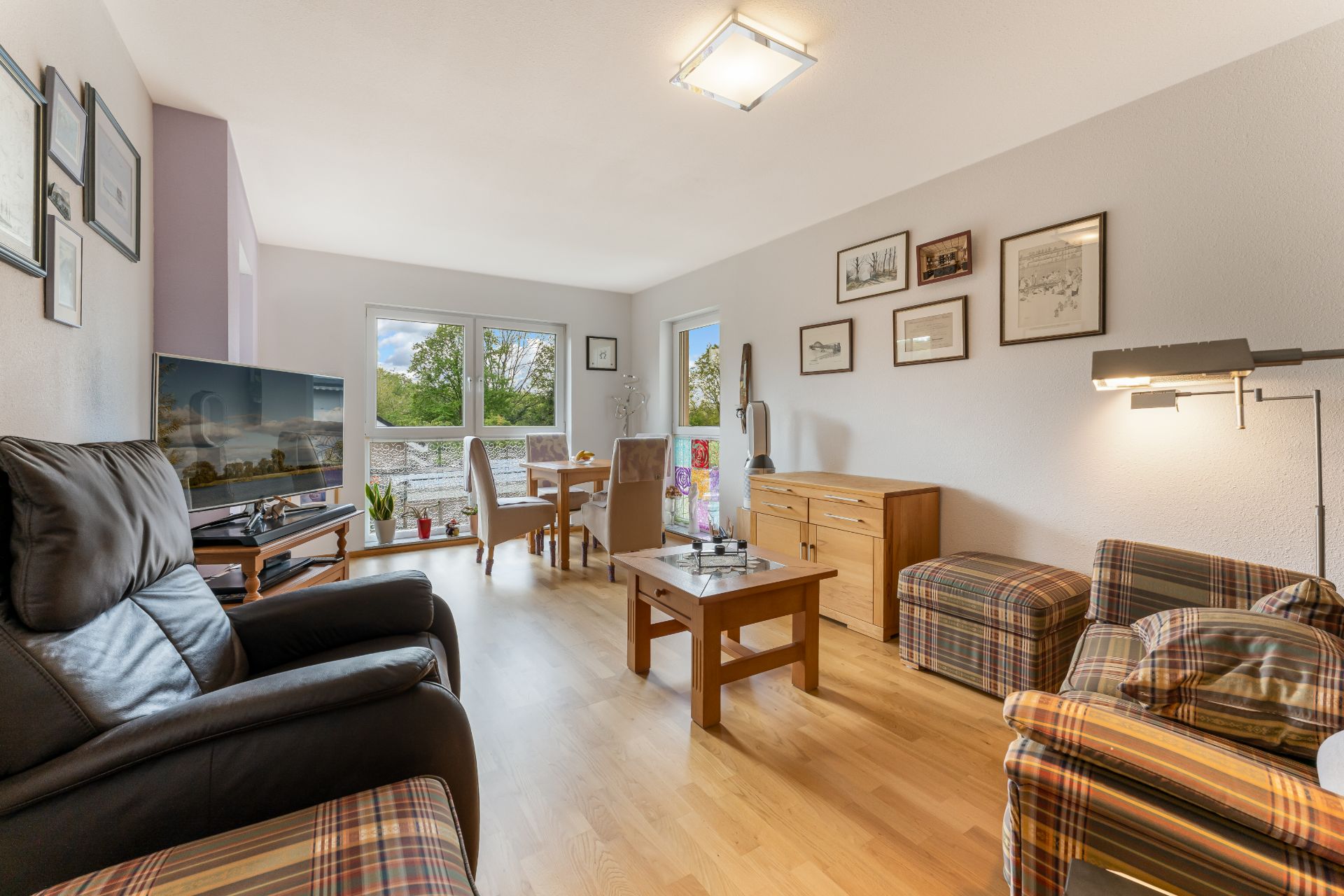 Helles Wohnzimmer mit Ledersessel, Couchtisch, Esstisch, großem Fenster und dekorierten Wänden.