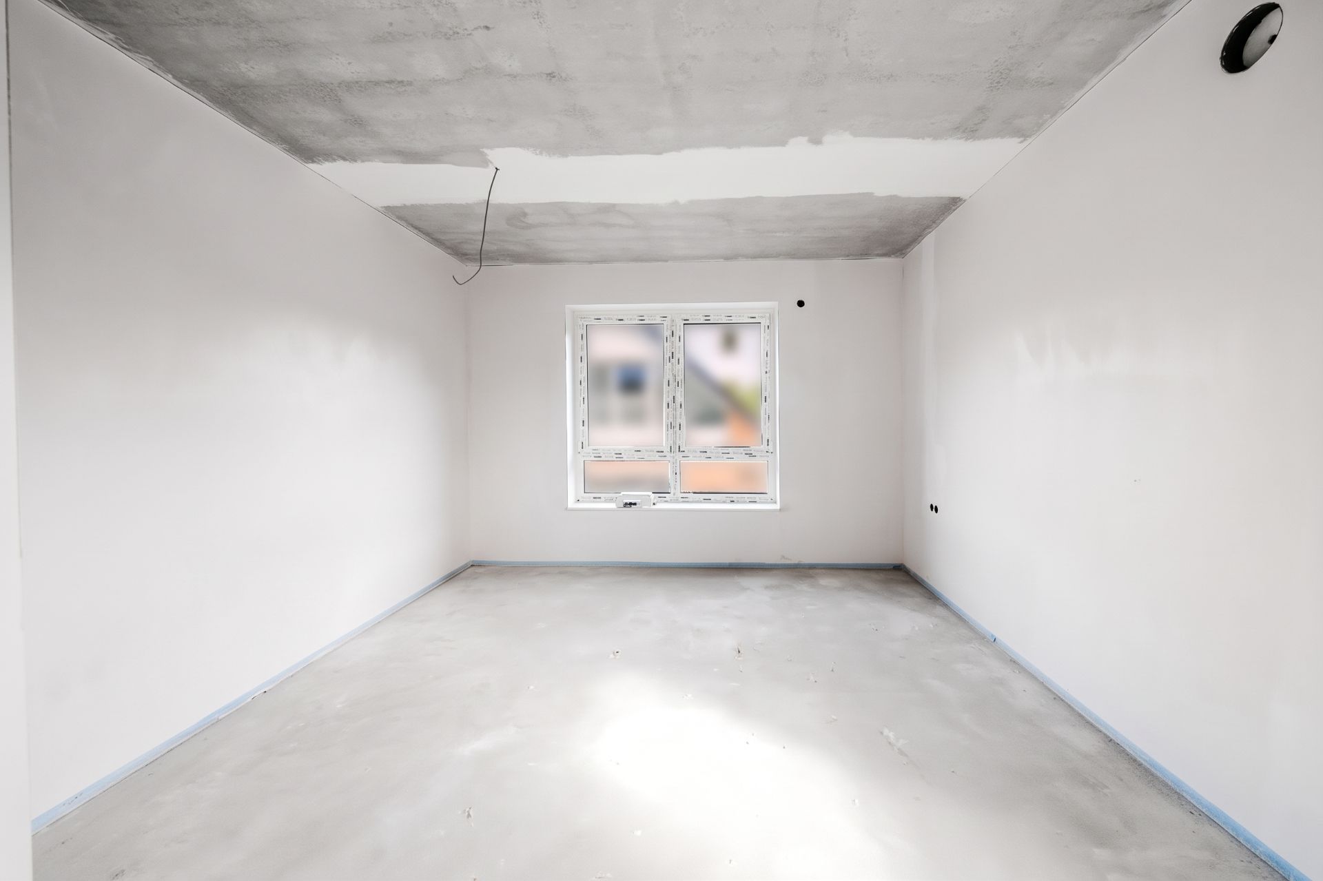 Leerer Raum mit weißen Wänden, grauem Boden und einem Fenster an der Stirnwand.
