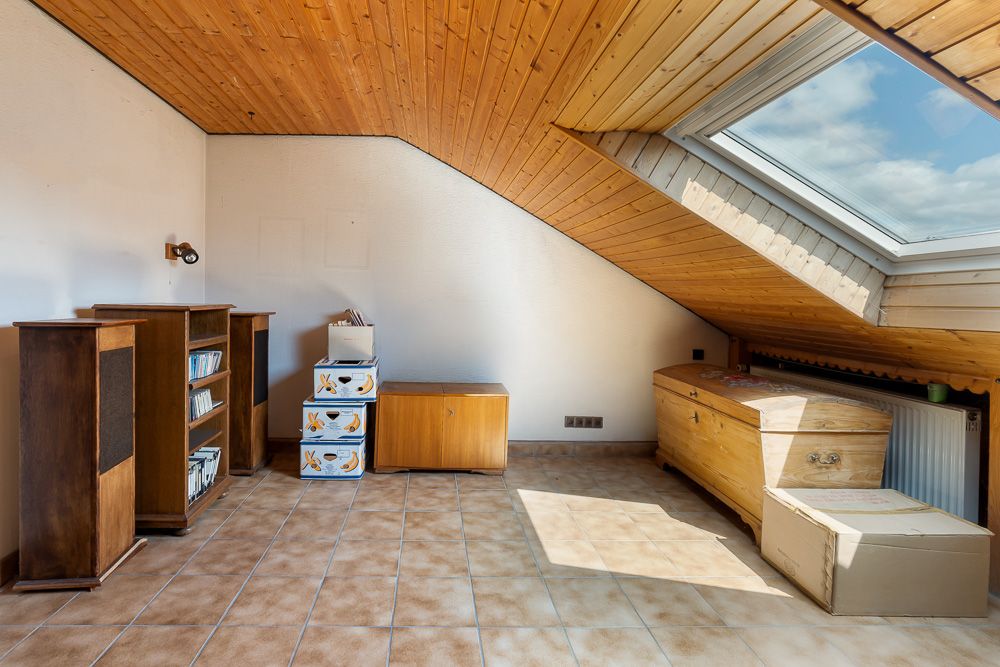 Dachzimmer mit Holzdecke, Schräge, Regalen, Kisten und großem Dachfenster.