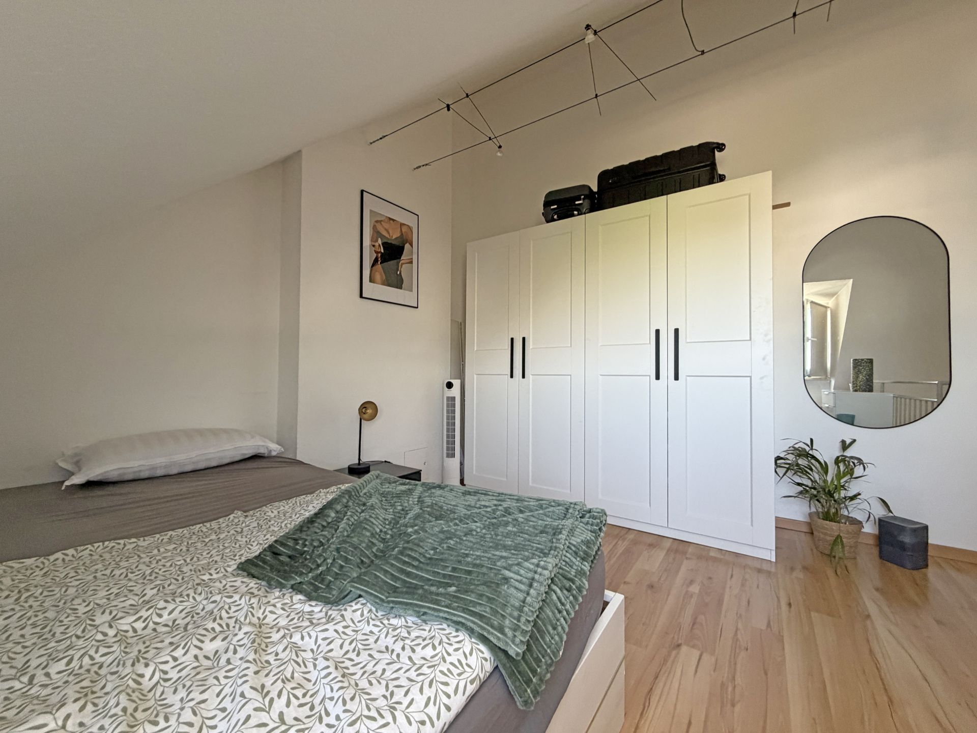 Schlafzimmer mit Bett, großem weißen Kleiderschrank, Spiegel und Holzboden.