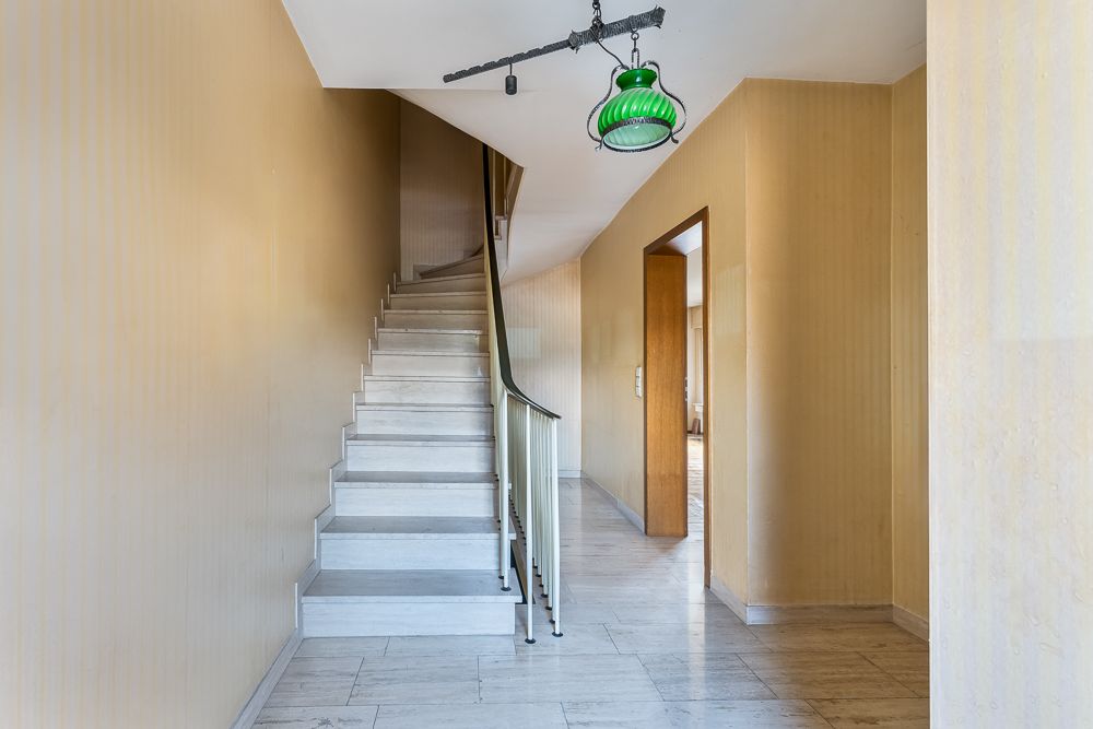 Heller Flur mit Marmortreppe und grünem Deckenlicht in einem Wohnhaus.