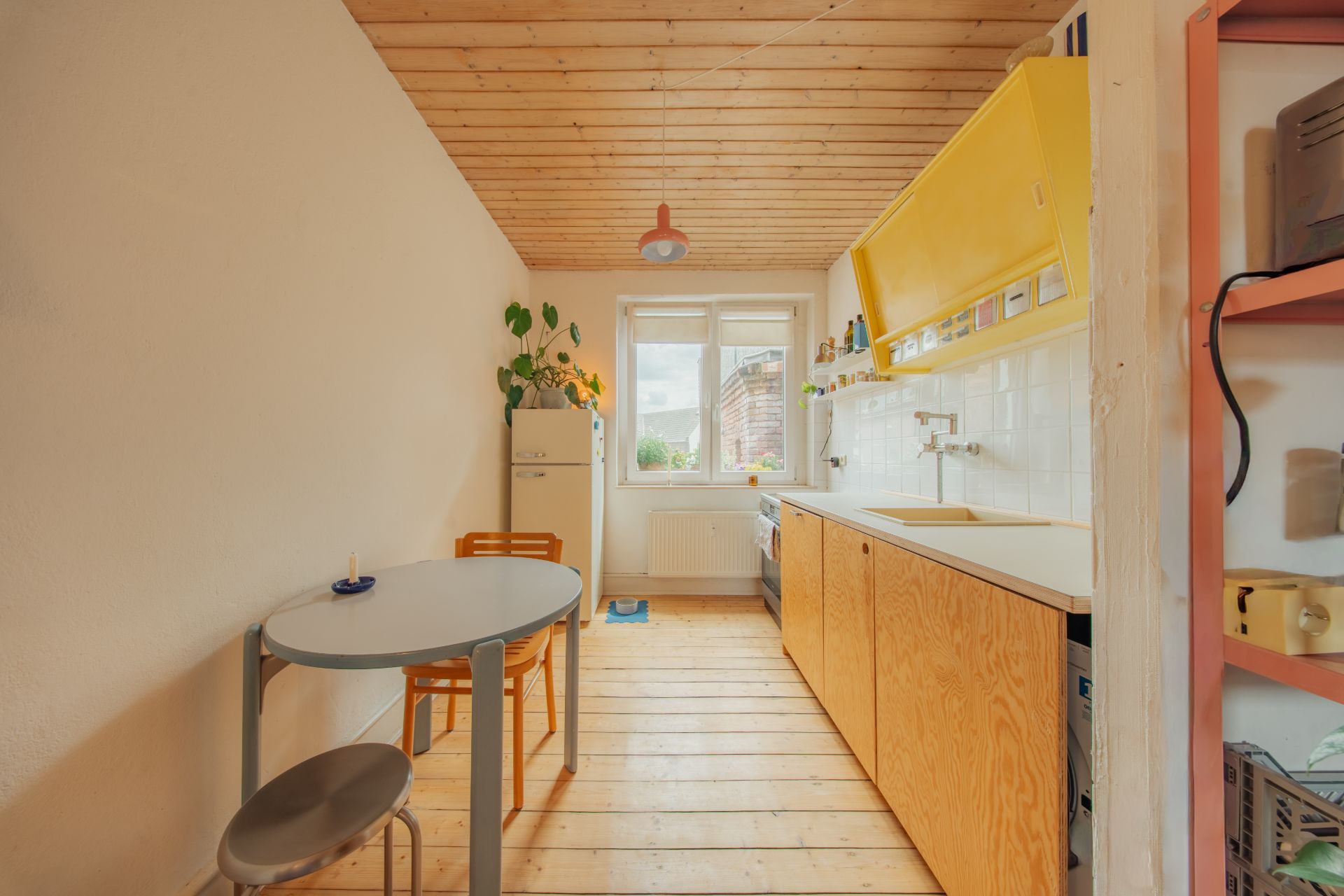 Helle Küche mit Holzboden, kleinem Esstisch, gelben Schränken und Fenster am Ende des Raums.