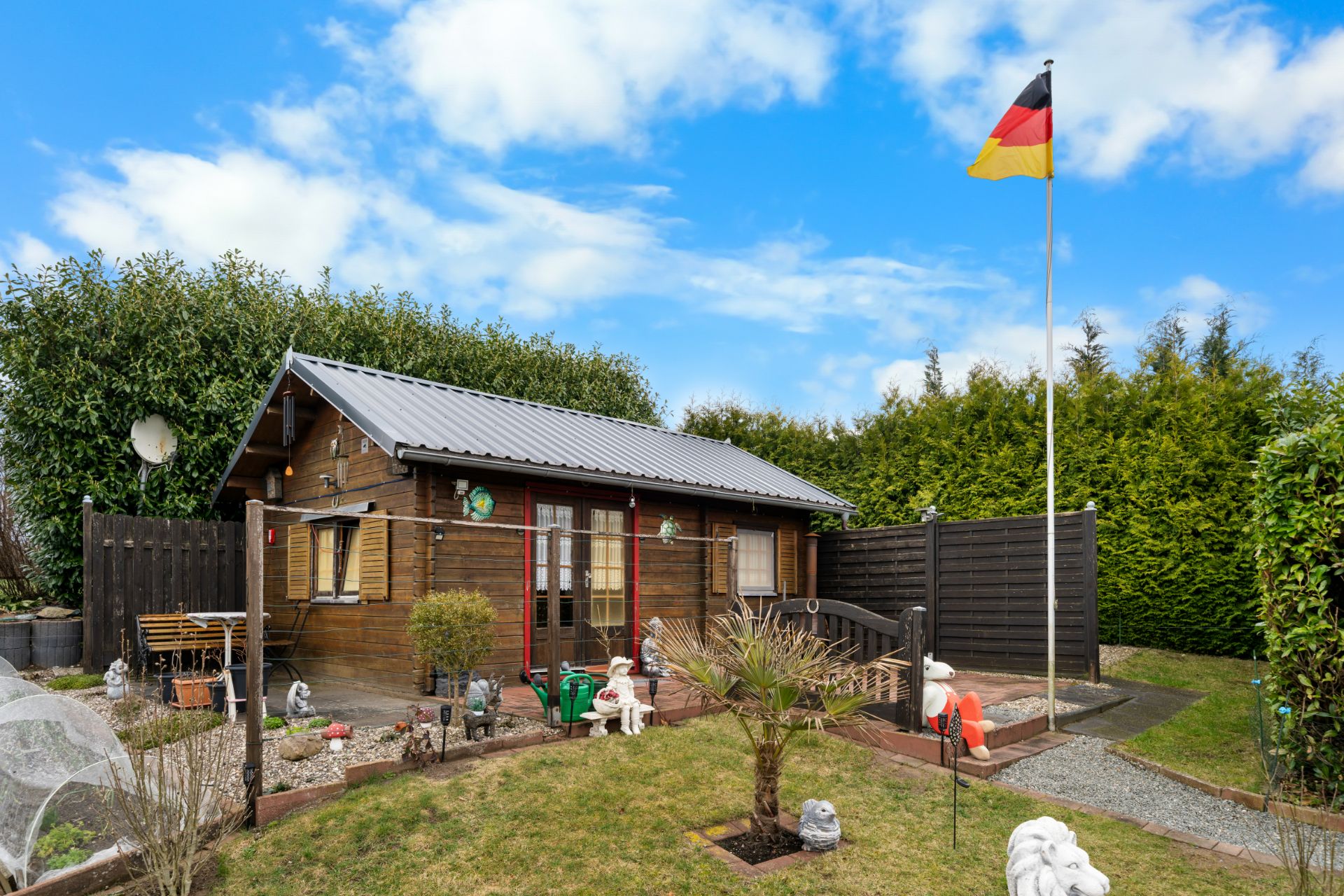 Holzhaus mit Garten, Rasenfläche, Gartendekorationen und deutscher Flagge im Vordergrund.