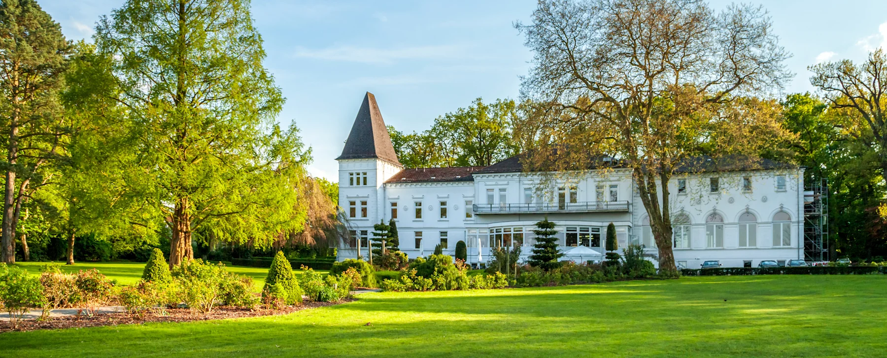 Großes weißes Wohngebäude mit Turm, umgeben von Rasen und Bäumen.