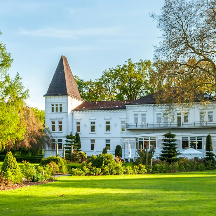 Großes weißes Wohngebäude mit Turm, umgeben von Rasen und Bäumen.