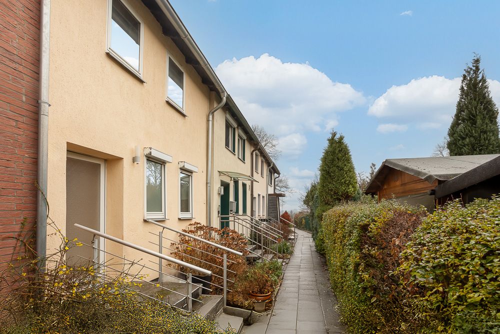 Reihenhaus mit gelber Fassade, Treppenaufgang und Gehweg, umgeben von Büschen.