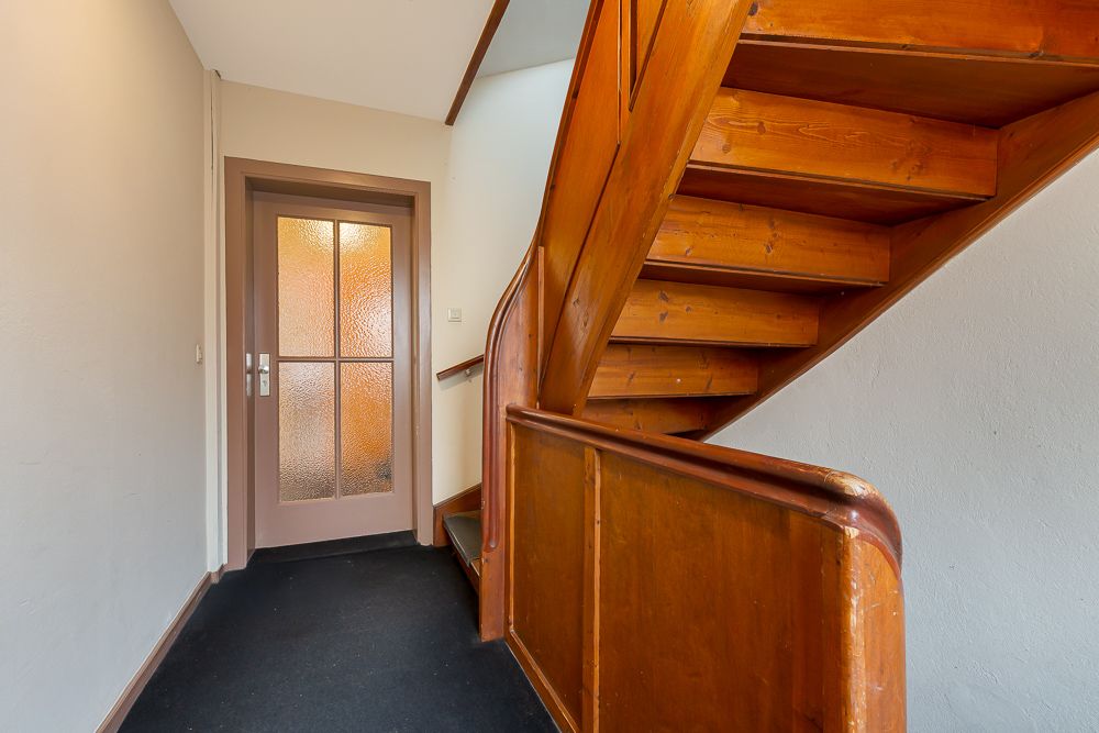 Holztreppe mit Geländer neben einer Glastür in einem Flur.