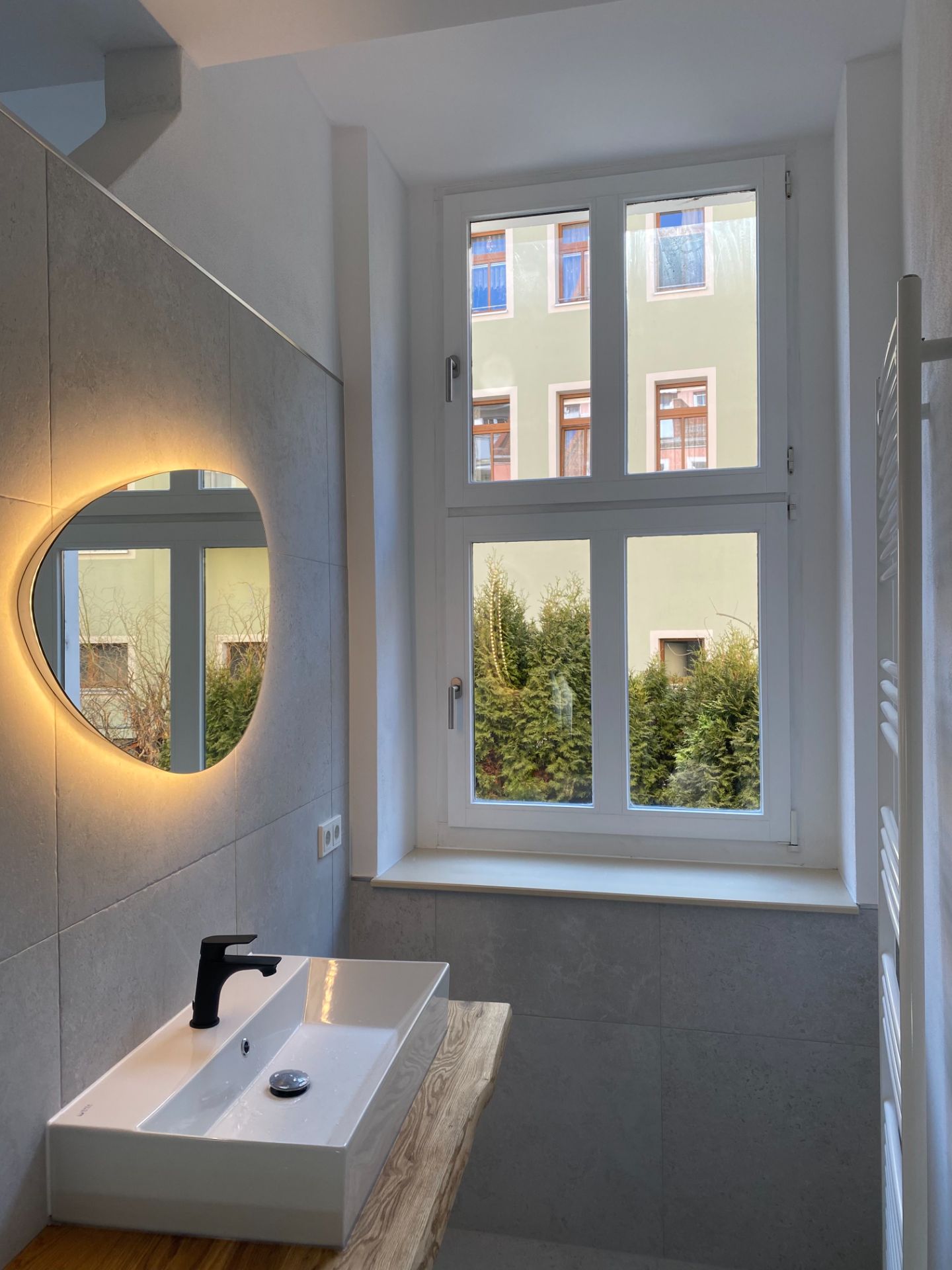 Modernes Bad mit Fenster, beleuchtetem Spiegel und Waschbecken auf Holzplatte.