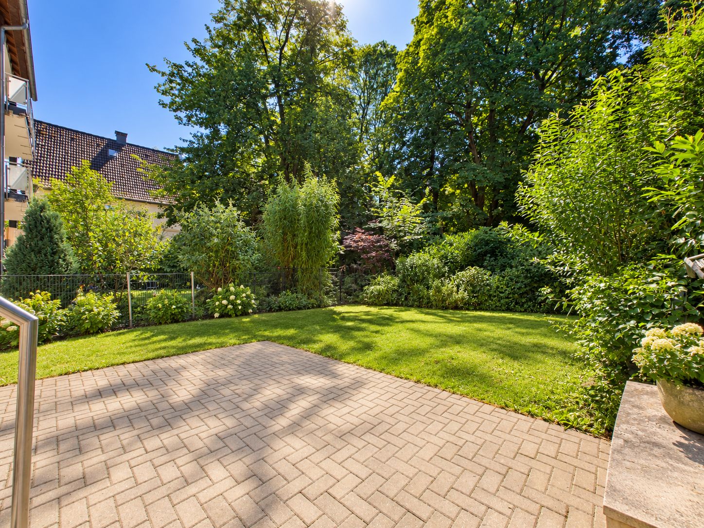Sonnige Terrasse mit Blick auf einen grünen Garten und viele Bäume im Hintergrund.