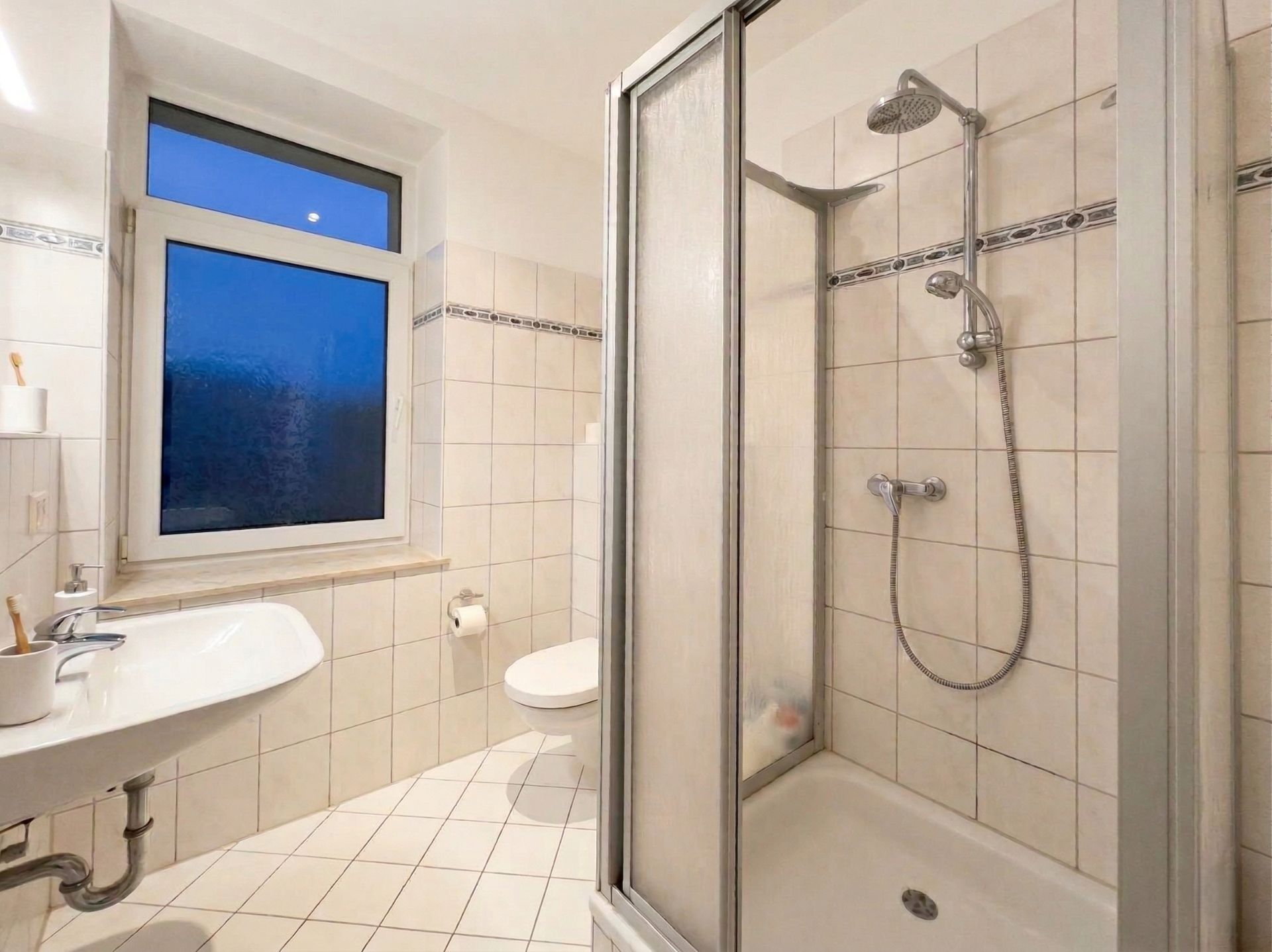 Helles Badezimmer mit Dusche, WC, Waschbecken und Fenster mit Milchglas.