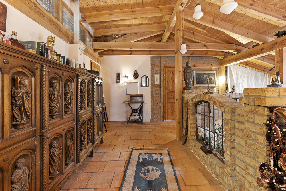 Flur mit Holzbalkendecke, Ziegelwänden, Teppich und geschnitztem Holzschrank, dekoriert mit Statuen.