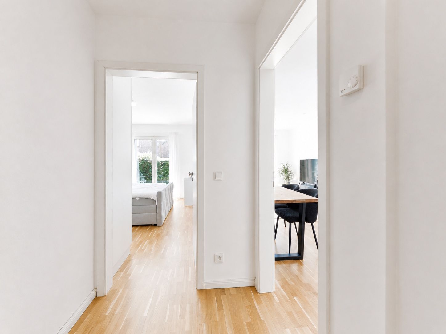Heller Flur mit Holzboden, Blick in ein Wohnzimmer und ein weiteres Zimmer mit Sofa.