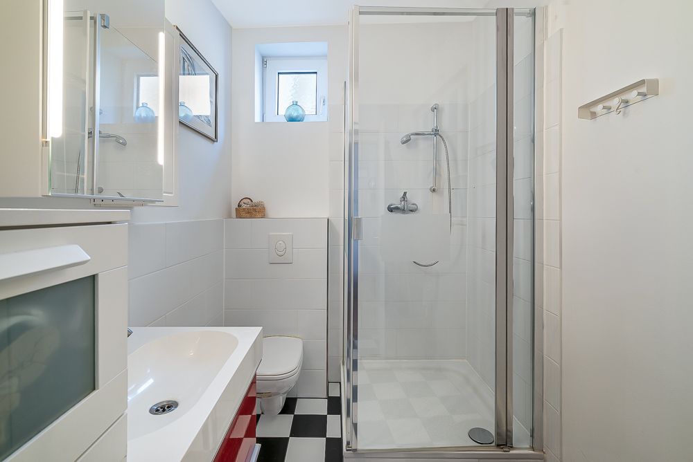 Modernes Badezimmer mit Dusche, Waschbecken, Toilette und kleinem Fenster.