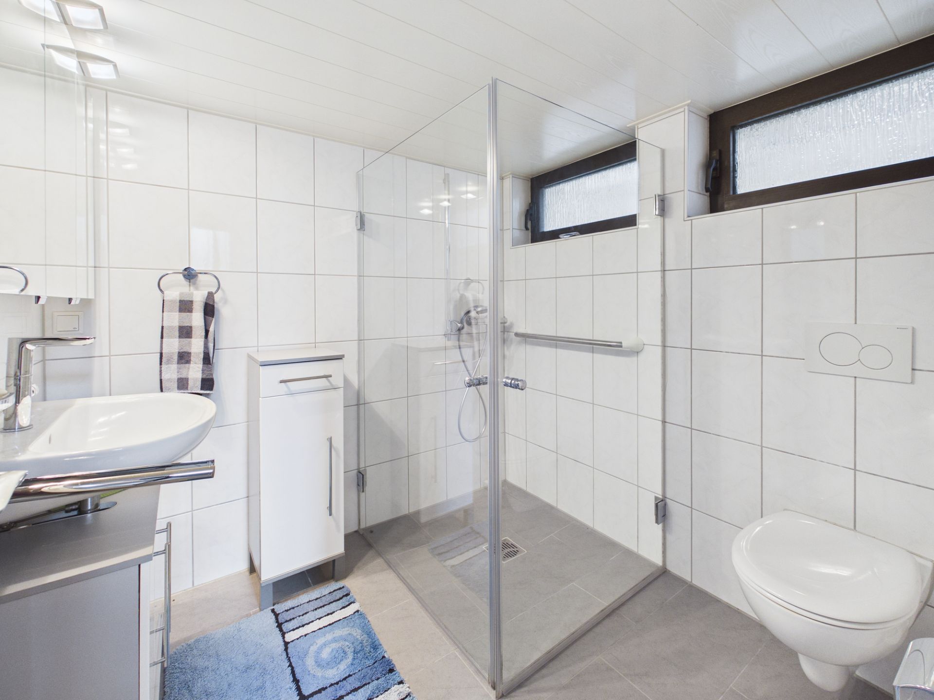 Modernes Badezimmer mit ebenerdiger Dusche, Waschbecken, WC und weißen Fliesen.