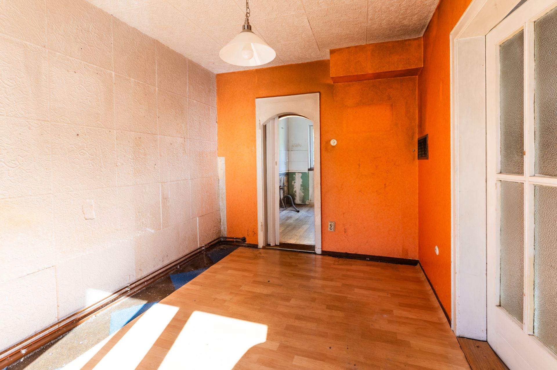 Leerer Raum mit Holzboden, orangefarbener Wand und Tür zu einem weiteren Zimmer.