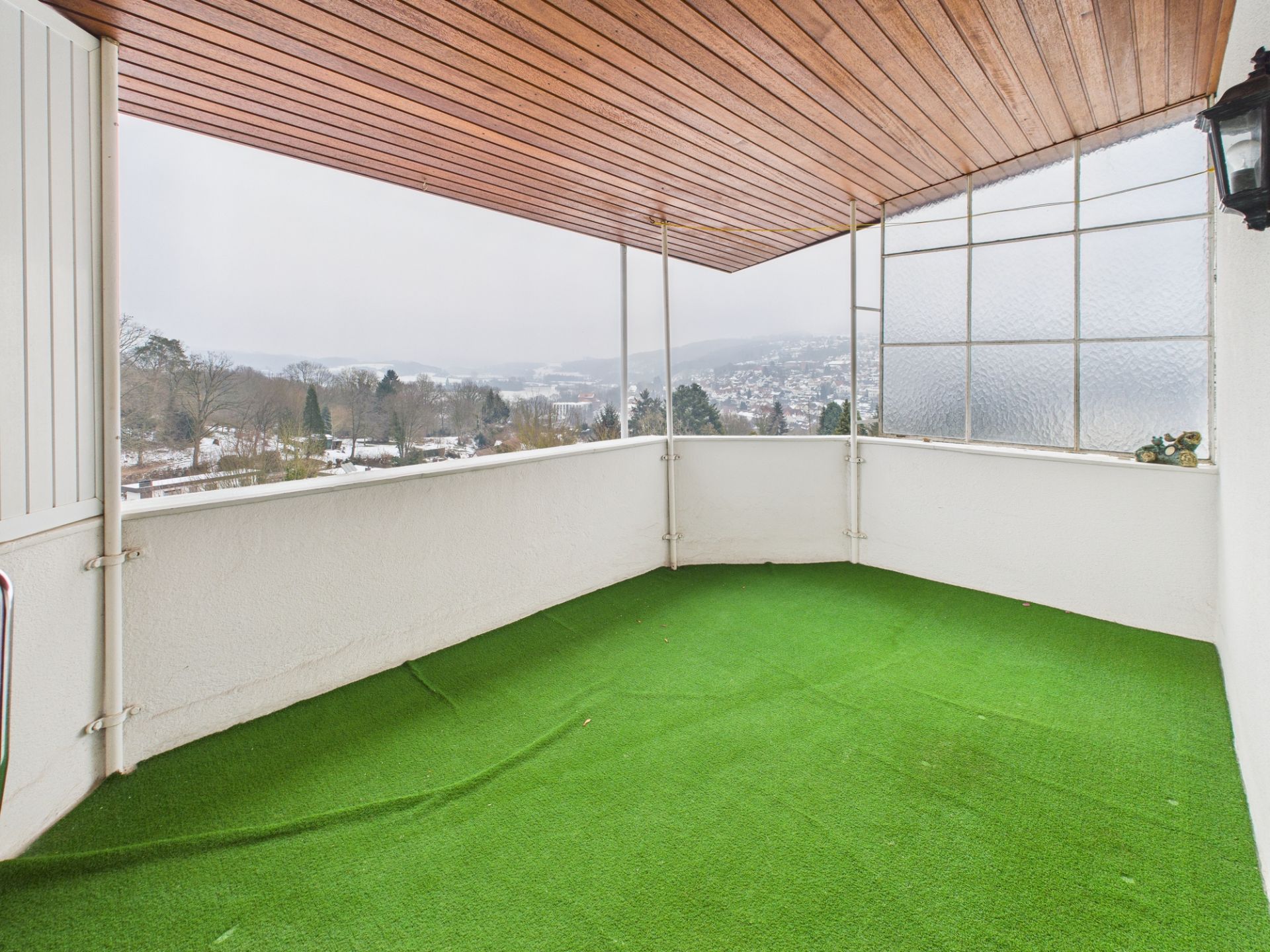 Überdachter Balkon mit grünem Bodenbelag und Blick auf eine hügelige Landschaft.