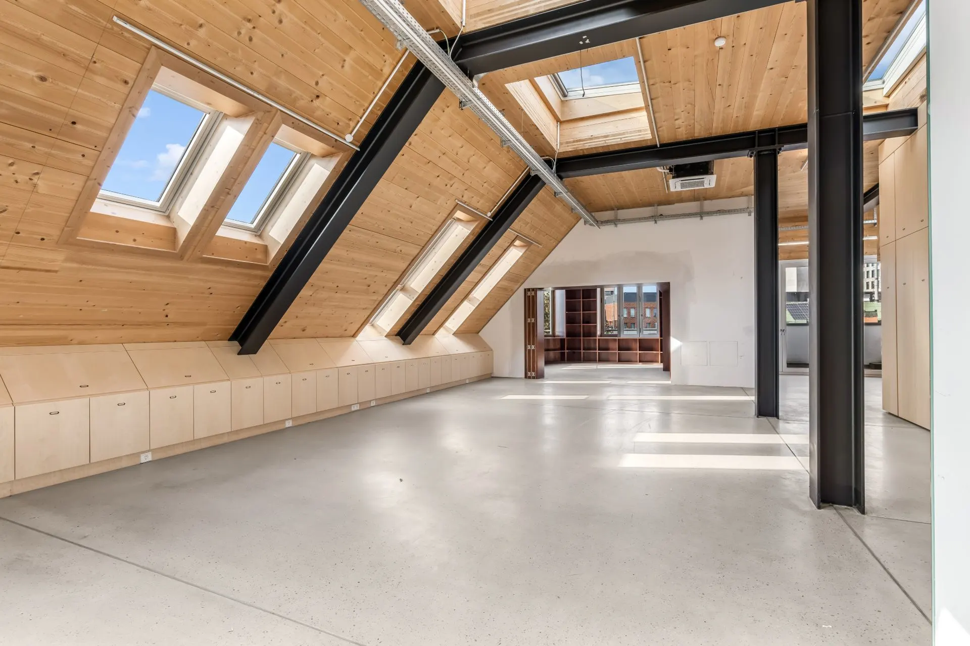 Geräumiges Zimmer mit schrägen Holzdecken, Fenstern und Einbauschränken unter dem Dach.