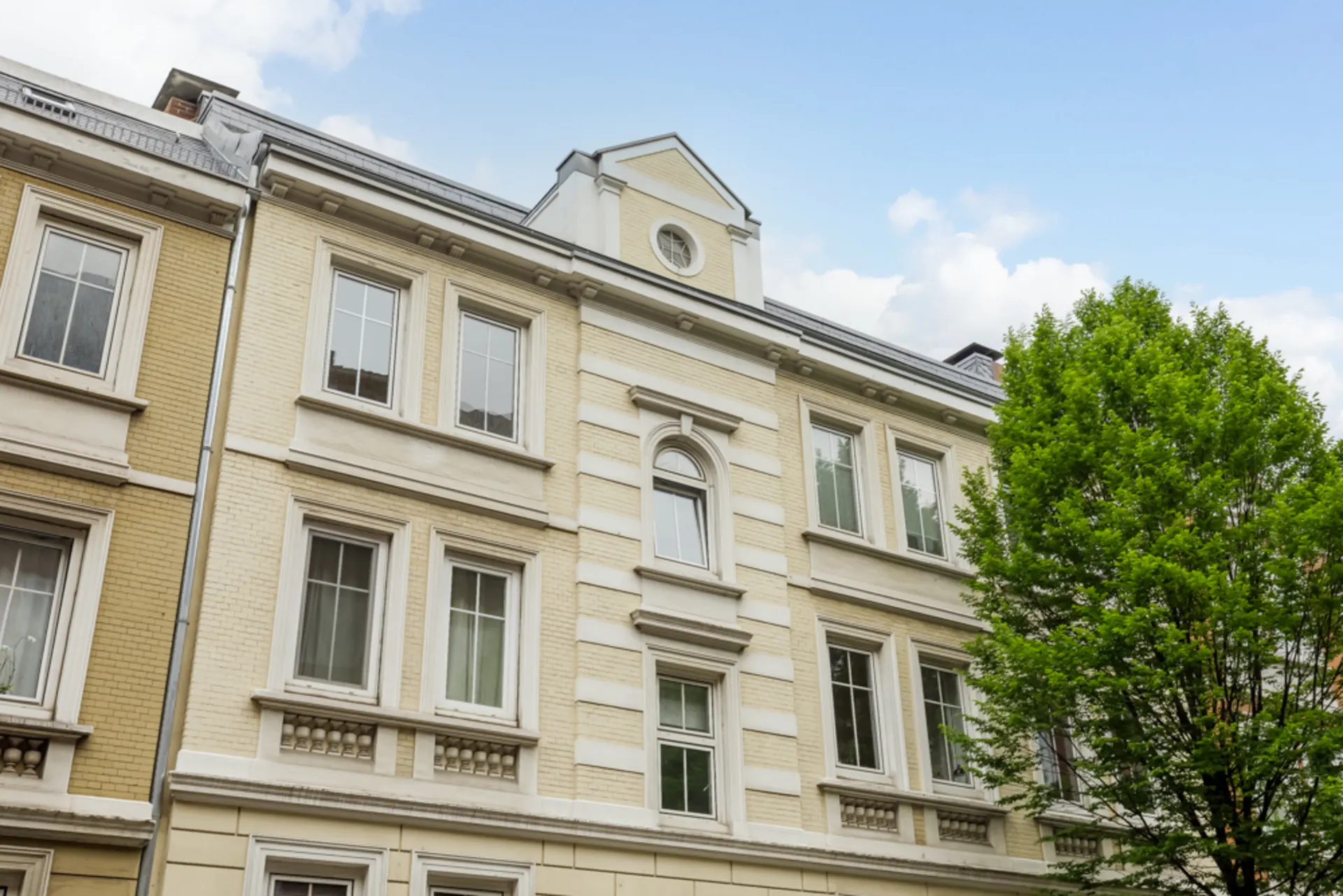 Fassade eines mehrstöckigen Wohnhauses mit großen Fenstern und Baum davor.