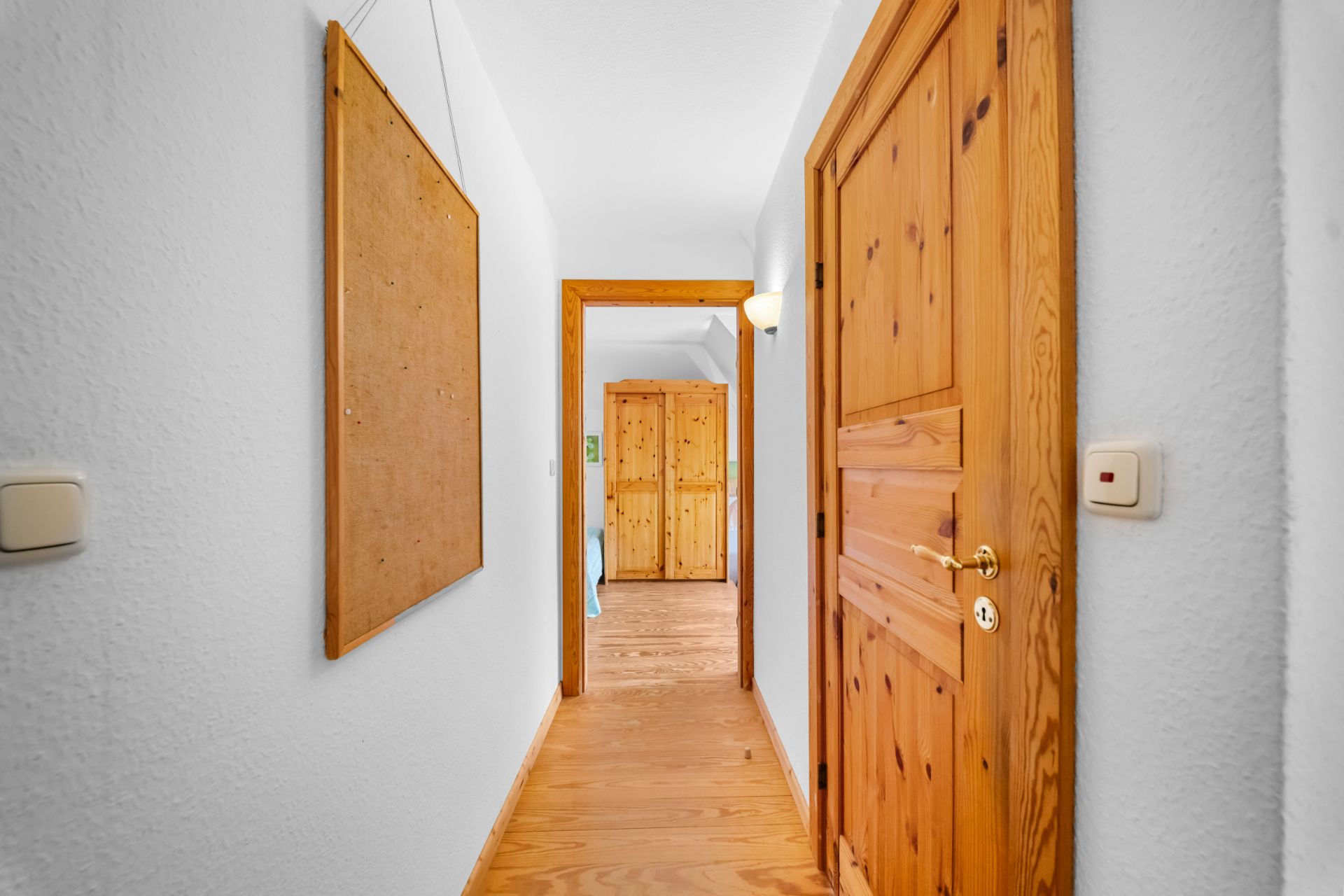 Langer Flur mit Holztüren, Holzfußboden und Pinnwand, am Ende ein Kleiderschrank.
