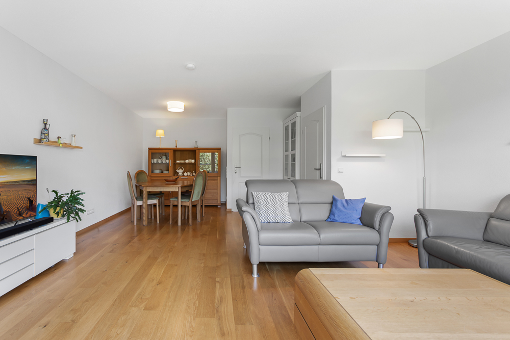 Helles Wohnzimmer mit Holzboden, grauen Sofas und Essbereich mit Holztisch und Stühlen.