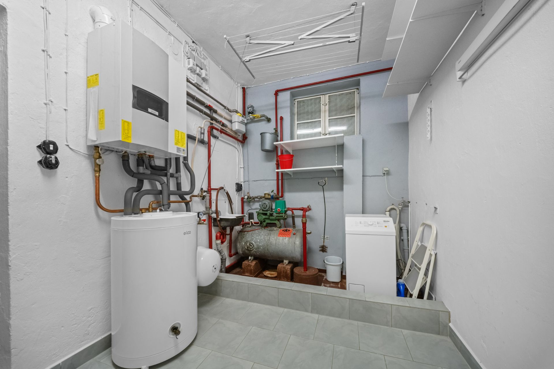 Heizungsraum mit Boiler, Rohren, Waschmaschine und Fenster.