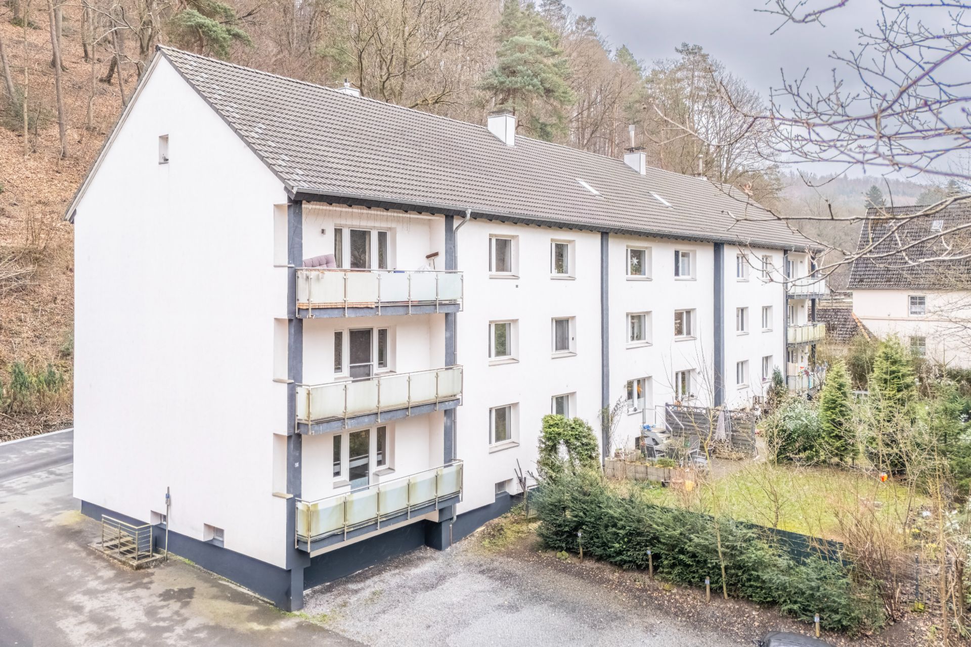Dreistöckiges Wohnhaus mit mehreren Balkonen und einem kleinen Garten an der Seite.