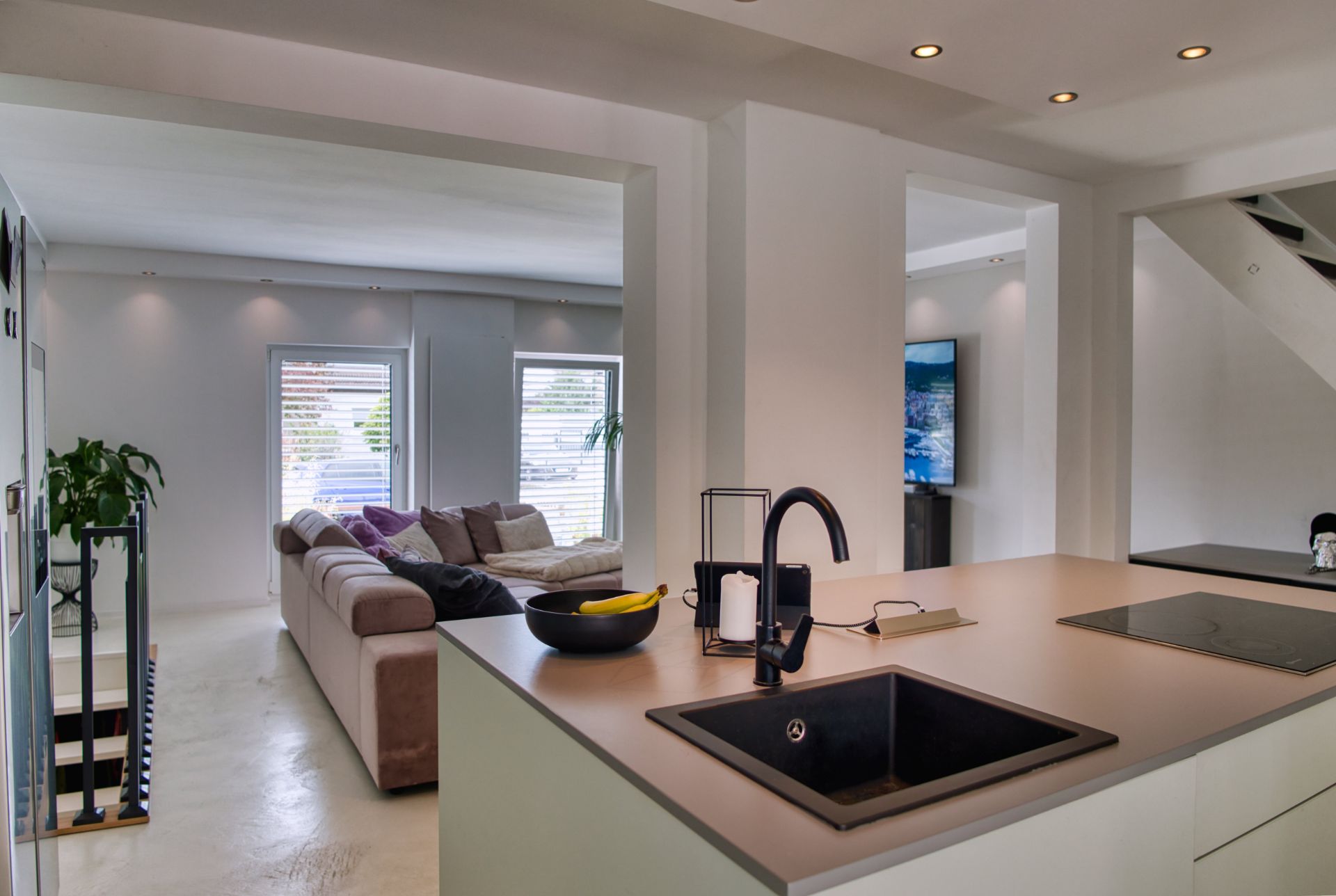 Helle, moderne Küche mit Spüle und Wohnzimmer mit Ecksofa im Hintergrund.