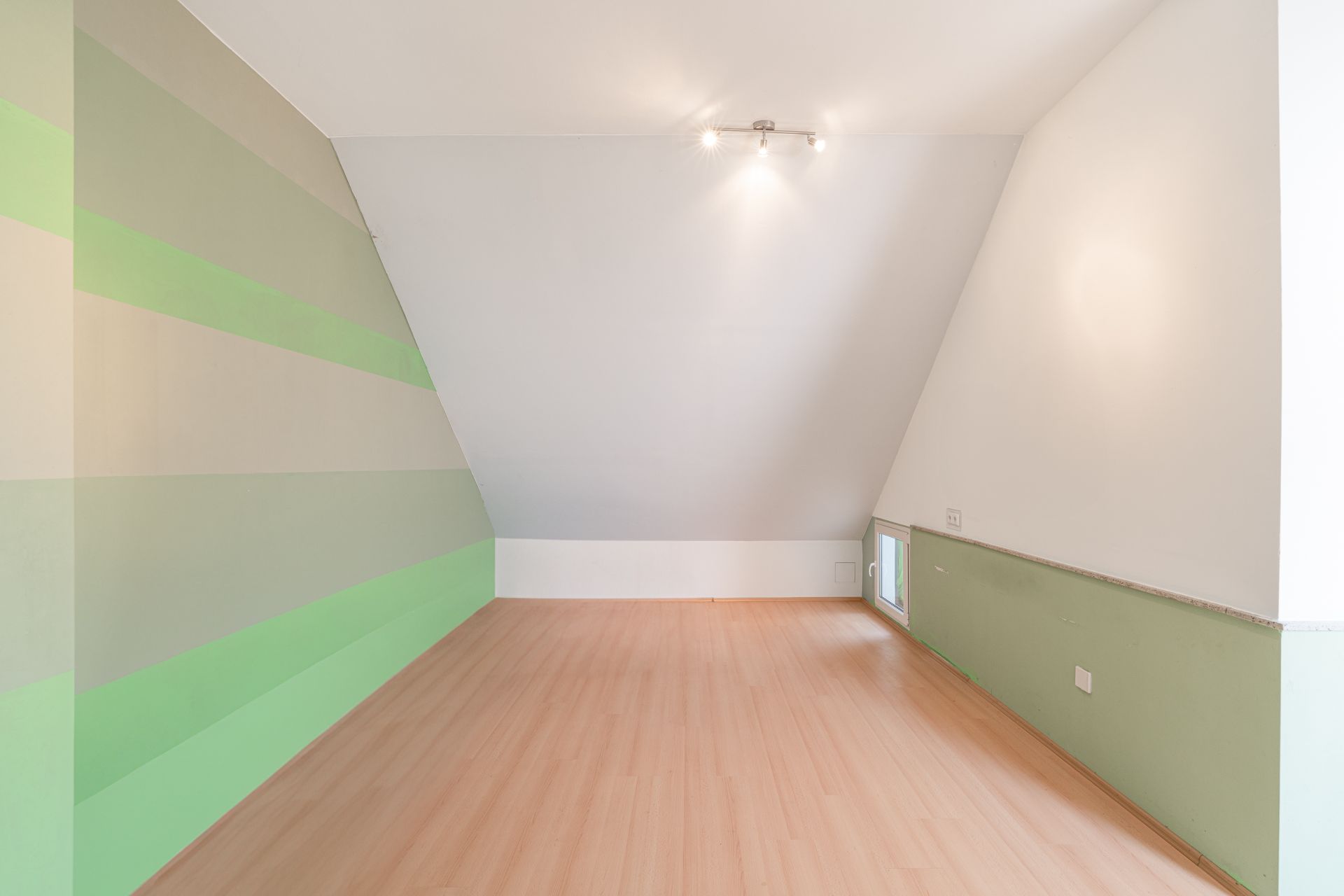Helles Dachzimmer mit schrägen Wänden, Holzfußboden und grün gestreifter Wand.