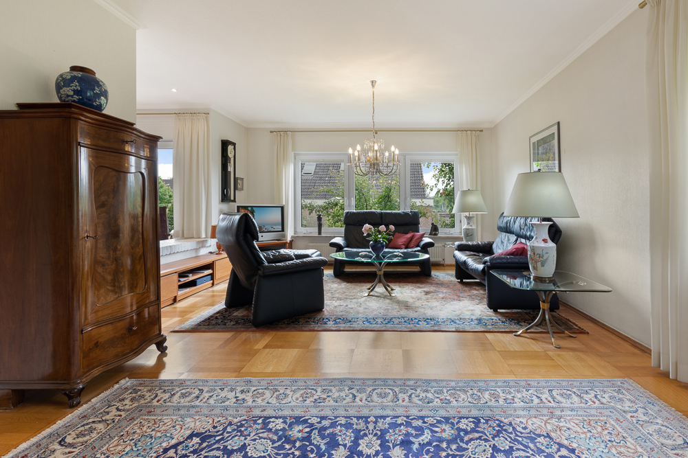Wohnzimmer mit Ledersofas, Holzboden, Teppichen, Kronleuchter und großen Fenstern.