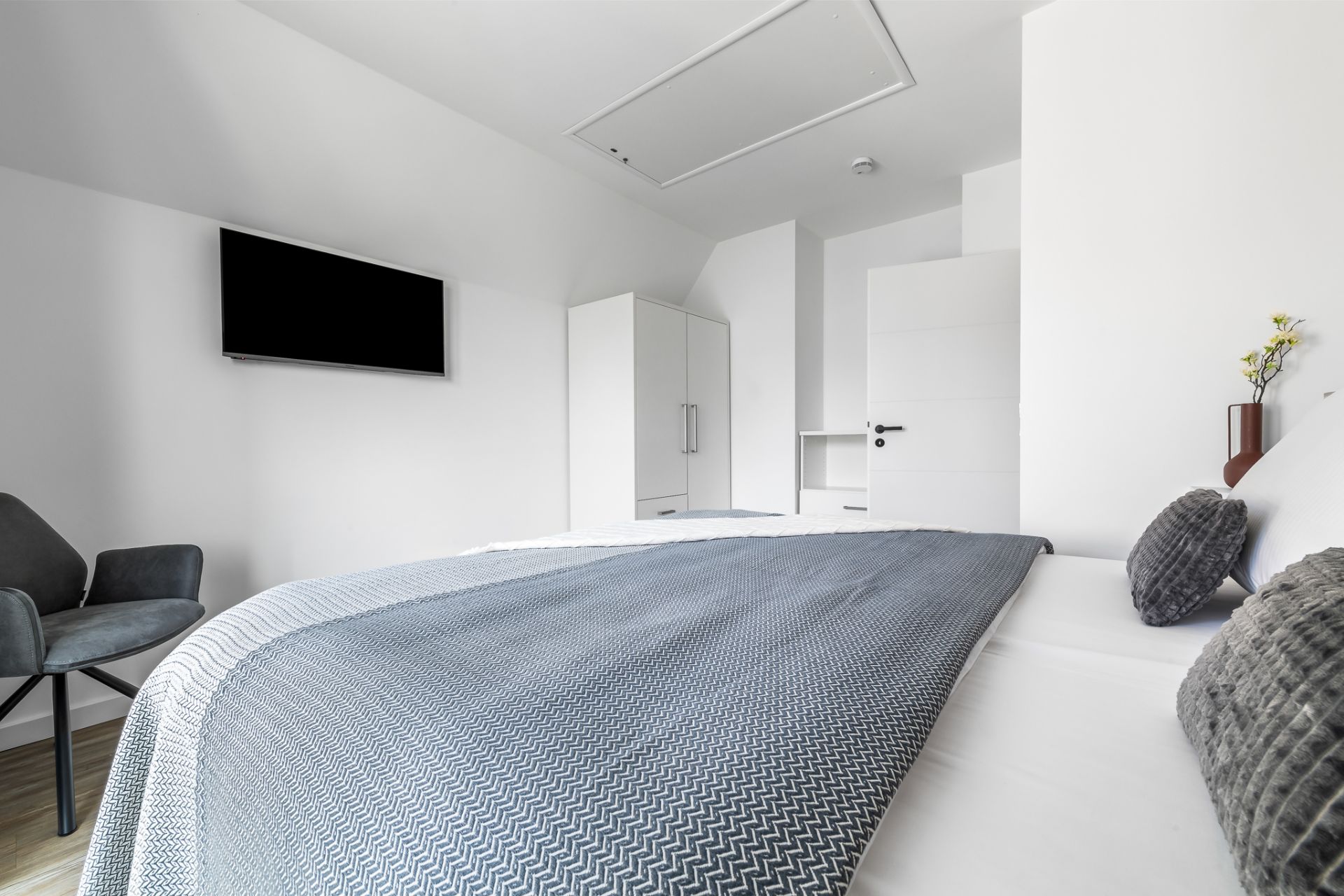 Modernes Schlafzimmer mit Doppelbett, grauer Decke, TV an der Wand und weißem Kleiderschrank.
