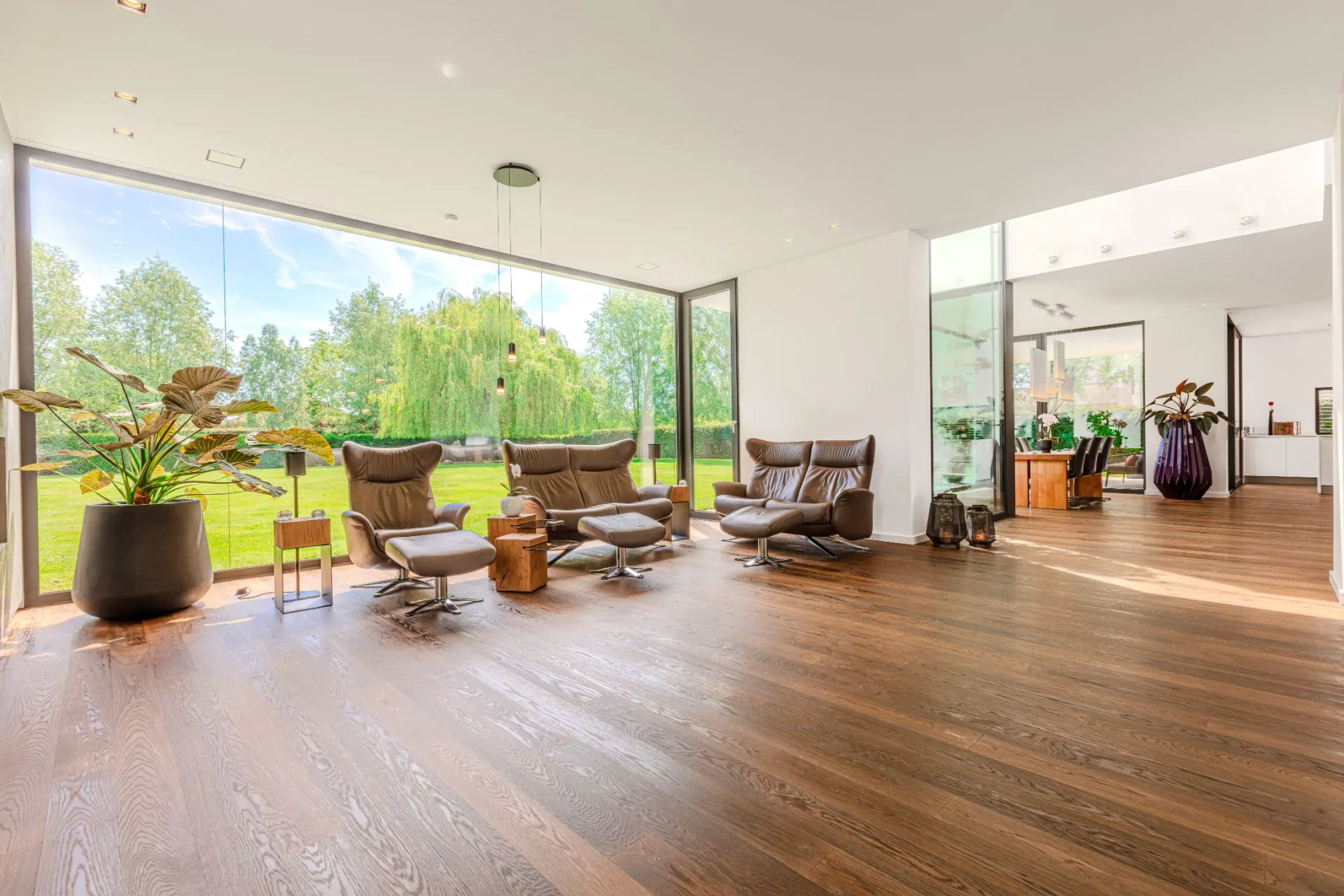 Helles Wohnzimmer mit braunen Sesseln, großen Fenstern und Holzboden, Blick auf den Garten.