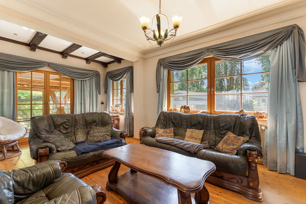 Wohnzimmer mit Ledersofas, Holztisch, großen Fenstern und blauen Vorhängen.