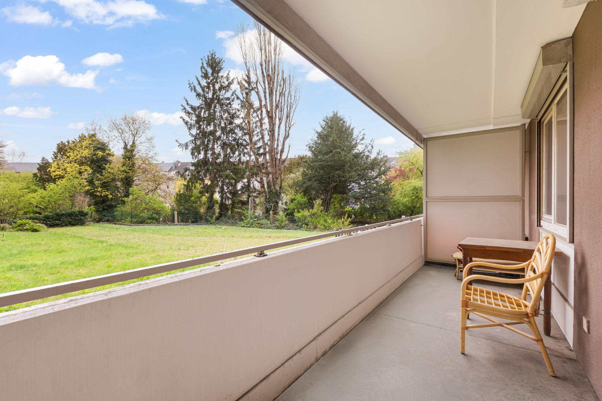 Überdachter Balkon mit zwei Stühlen und Tisch, Blick auf grünen Garten und Bäume.