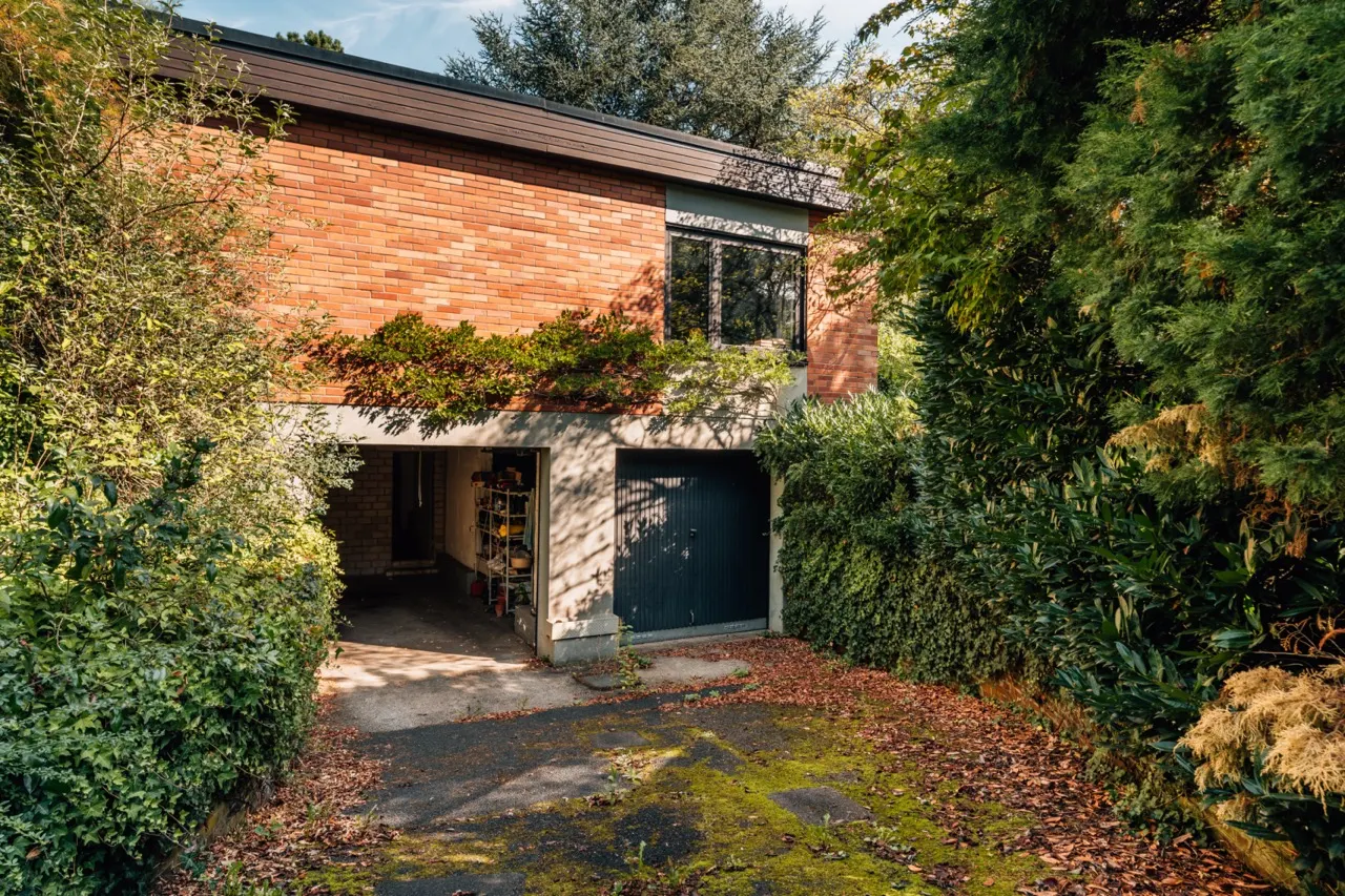 Backsteinhaus mit Garage, von viel Grün und Bäumen umgeben.
