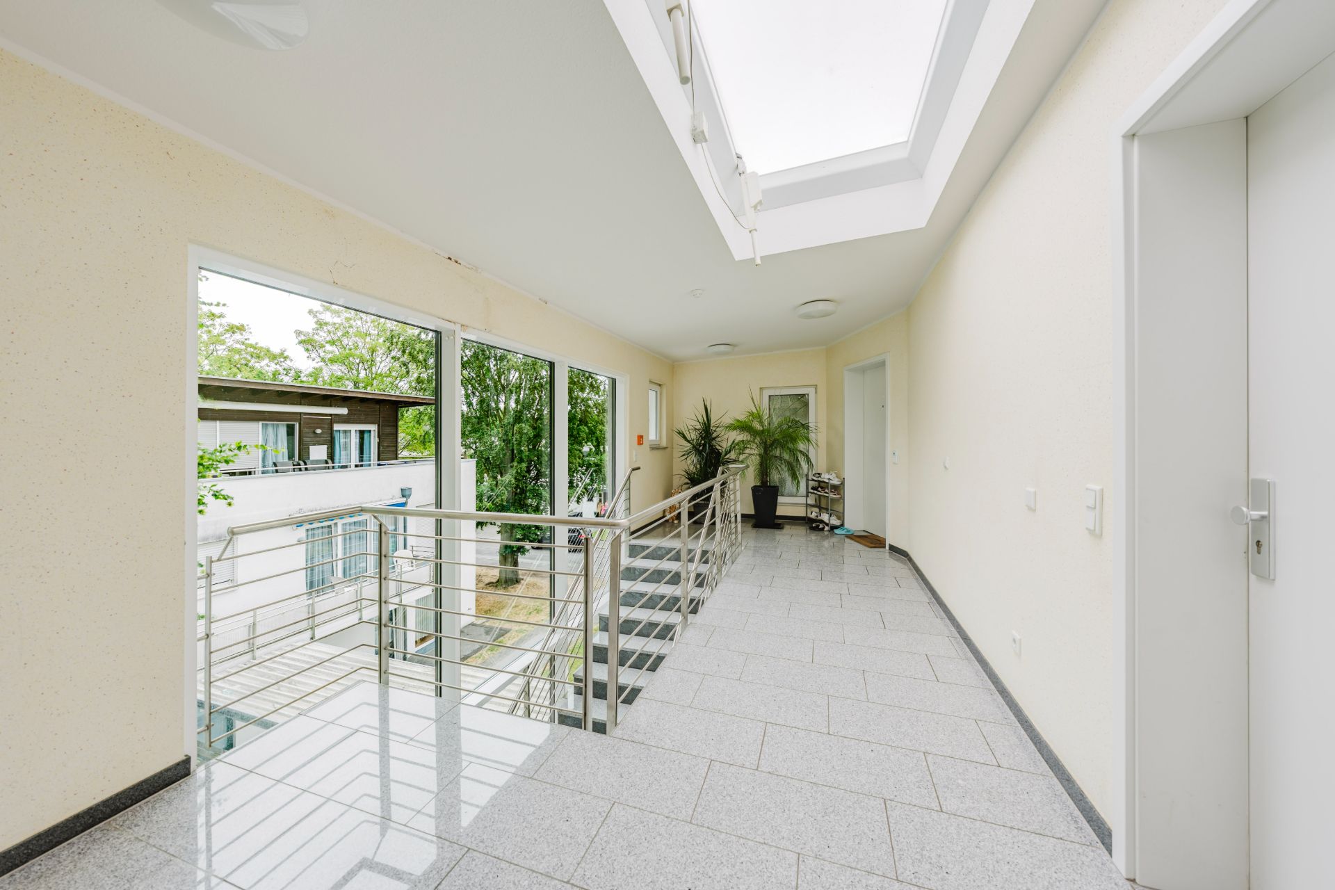 Heller Flur mit Treppe, großen Fenstern und Pflanzen in einem Wohnhaus.