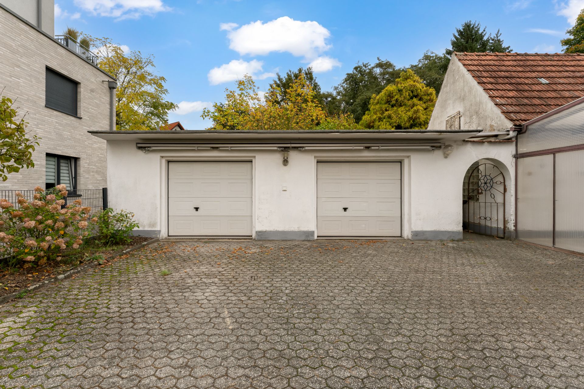 Zwei geschlossene Garagentore an einem weißen Gebäude mit gepflastertem Hof davor.