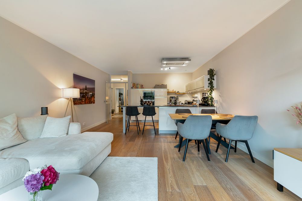 Modernes Wohnzimmer mit offener Küche, Esstisch, grauem Sofa und Holzfußboden.