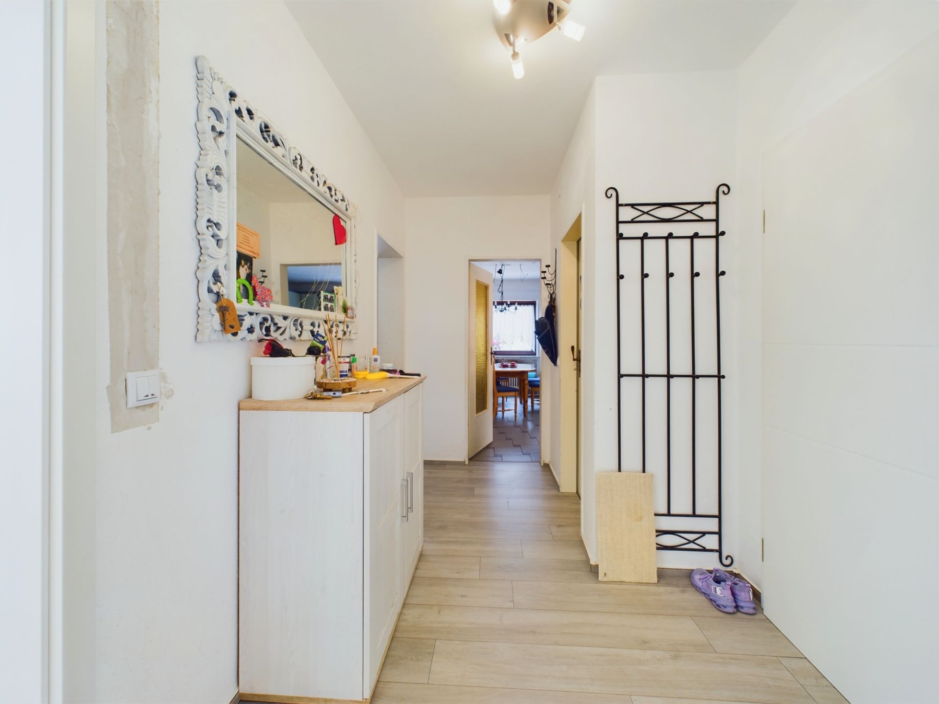 Heller Flur mit Spiegel, Kommode und Wandgarderobe, Blick in ein Esszimmer.