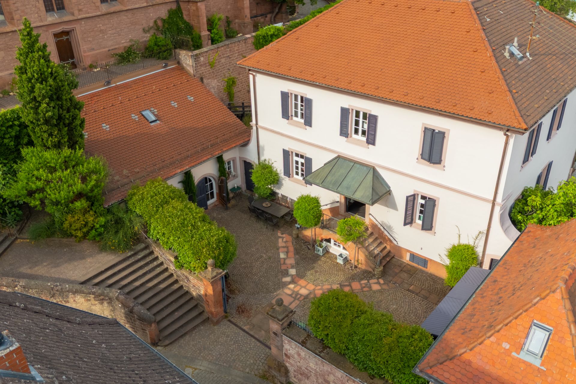 Innenhof mit weißem Wohnhaus, Nebengebäude, Sitzbereich und Treppen, umgeben von Mauern und Pflanzen.