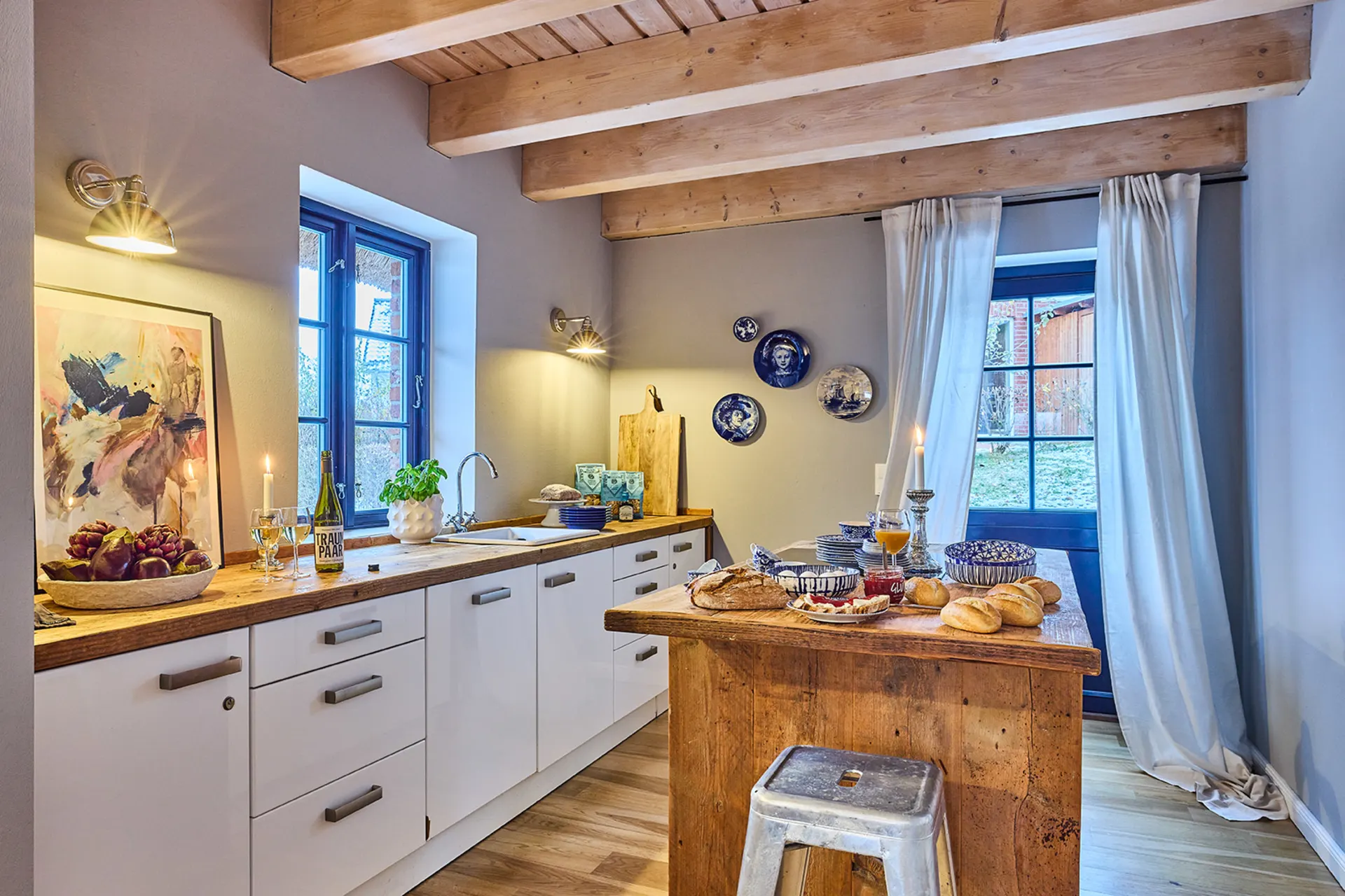 Gemütliche Küche mit Holzbalkendecke, Esstisch, weißem Schrank und Dekorationen an der Wand.