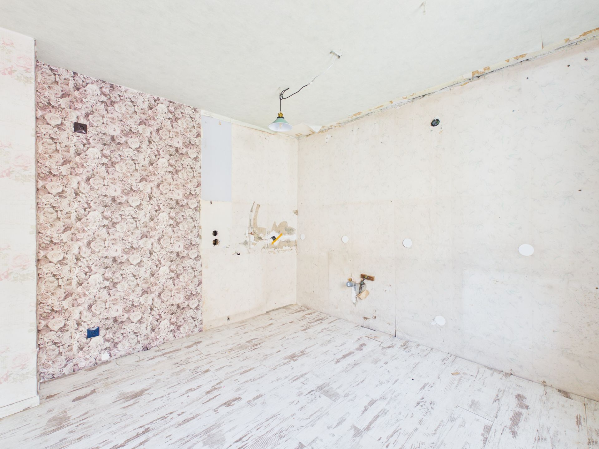 Leerer Raum mit abgenutztem Holzboden und floraler Tapete an einer Wand.