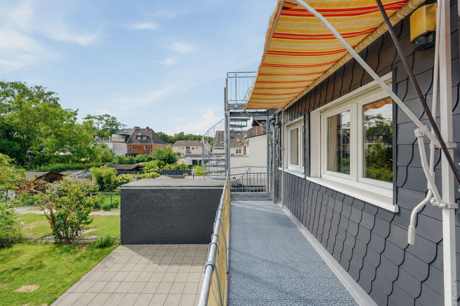Balkon mit Markise und Blick auf Garten und Nachbarhäuser an einem Wohngebäude.