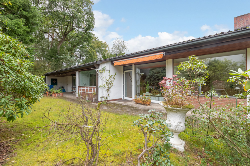Einfamilienhaus mit großer Fensterfront, Terrasse und Garten mit Pflanzen und Bäumen.